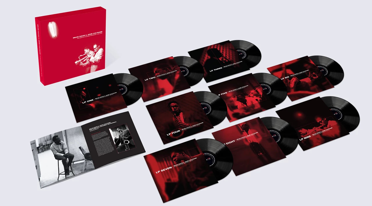Image of A vinyl record album set arranged on a light gray background, including a red outer box, multiple black LP records with red-and-black cover art, several album inserts, and an open booklet with a black-and-white photo.